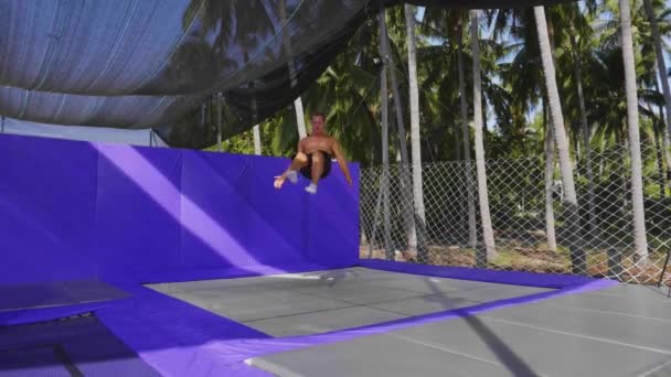 Мускулистый спортсмен делает кувыркание в воздухе, прыгая на батуте — стоковое видео