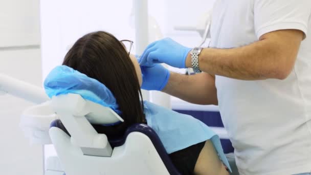 Стоматолог проводит профилактическое обследование женщины, сидящей на стоматологическом стуле — стоковое видео
