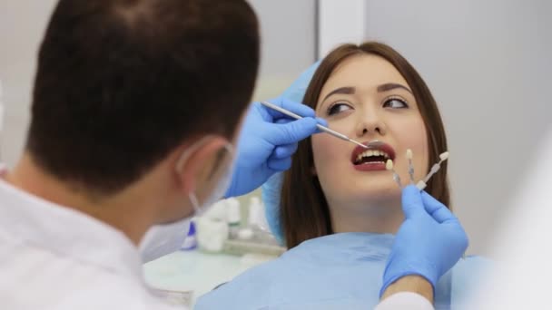 El dentista está eligiendo un color de diente de muestras para blanquear los dientes con láser — Vídeo de stock