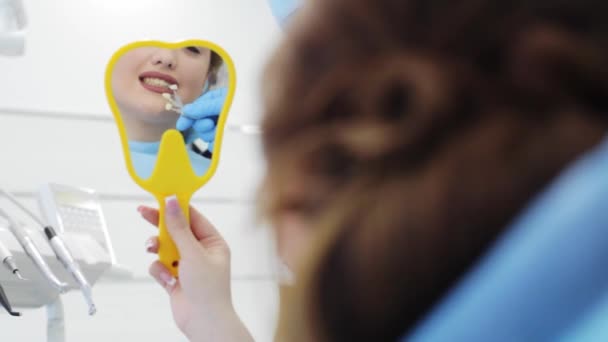 La mujer está mirando al espejo y eligiendo el color de los dientes de las muestras — Vídeo de stock