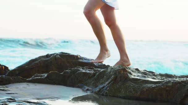 Mujer está caminando en la playa de arena del océano con piedras grandes, piernas de cerca . — Vídeos de Stock