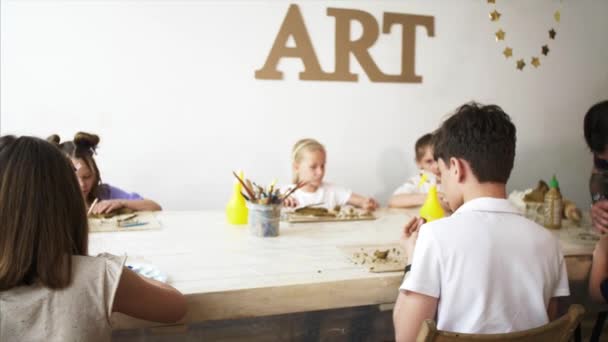 Kunstunterricht in der Werkstatt mit Kindern und Menschen, die ihnen das Formen aus Ton beibringen — Stockvideo