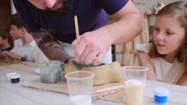 Sakallı öğretmen, öğrencisi kızına el yapımı oyuncaklarını kilden nasıl renklendireceklerini gösteriyor..