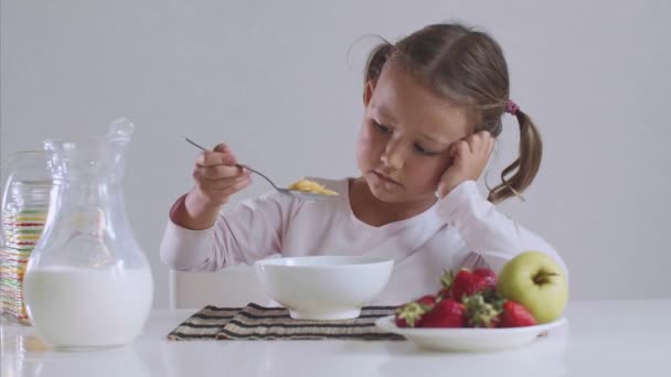 Pequena menina entediada não quer comer flocos de milho com leite para o café da manhã . — Vídeo de Stock