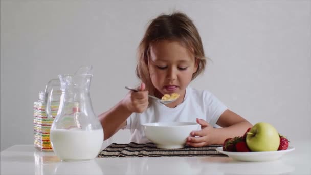 Pequeña niña linda come con placer copos de maíz con leche . — Vídeo de stock