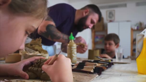 Художественный урок в мастерской с детьми и мужчиной, обучающий их лепить из глины — стоковое видео