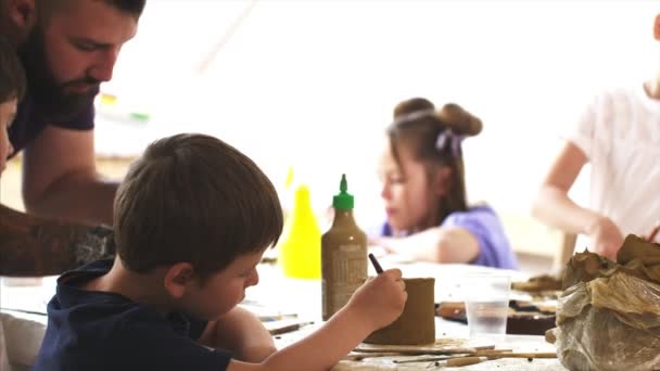 Lección de arte en taller con niños y hombres enseñándoles a esculpir de arcilla — Vídeo de stock