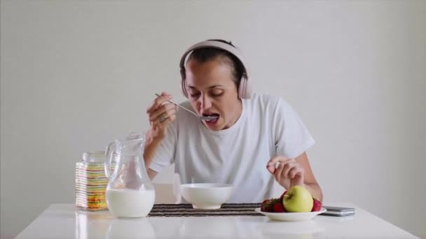 Mujer en auriculares está escuchando música mientras come copos de maíz con leche . — Vídeo de stock