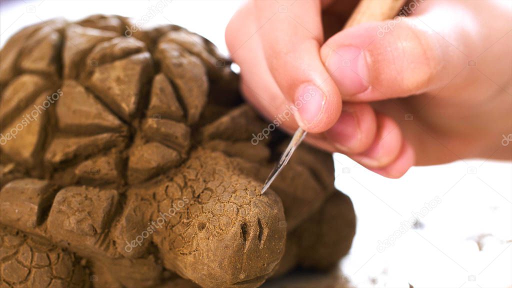 Child is scratching the texture of the scales on handmade turtle toy from clay