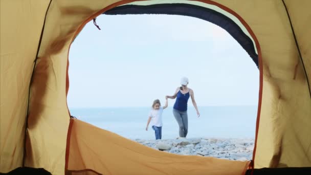 Jovem com sua filhinha entra na tenda de acampamento, descansando por mar . — Vídeo de Stock