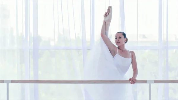 Professionelle Ballerina in weißem Tutu streckt ihre Beine in der Nähe des Ständers — Stockfoto