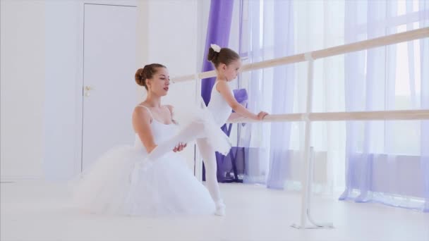 Professeur de ballet enseigne à la petite fille à étirer les jambes près du stand de barre . — Video