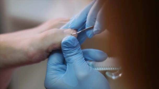 Pédicure dans les gants nettoie les ongles des orteils sur le pied des clients à l'aide d'un crochet métallique . — Video