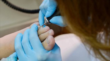 Mavi eldiven pedikür ustası güzellik salonunda donanım pedikür yapar.