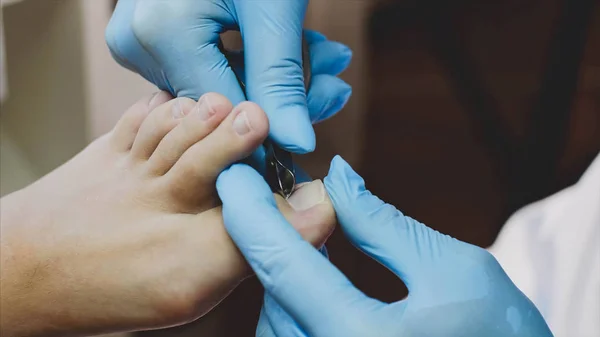 Pedicurist snijdt cuticula op teen met nagel tangen maakt pedicure in schoonheidssalon. — Stockfoto