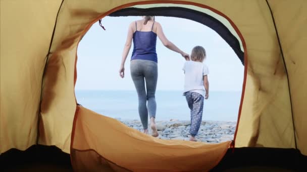 Mamma e figlia vanno al mare sulla spiaggia di pietre dalla tenda da campeggio tenendosi per mano . — Video Stock