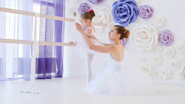 L'insegnante di danza sta insegnando alla bambina a sgranchirsi le gambe vicino allo stand della sbarra . — Foto Stock