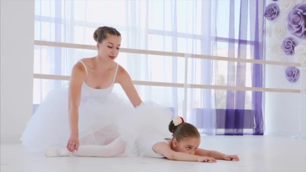 Pequeña bailarina en tutú blanco se estira en pose de rana con profesor de ballet . — Vídeos de Stock