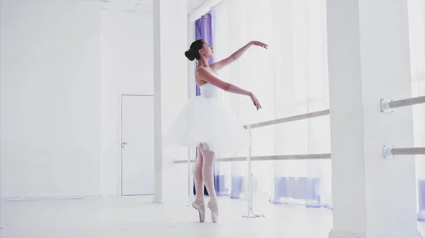 Ballerina in white tutu and pointes is dancing in ballet class.