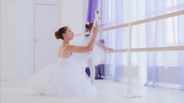 Bale öğretmeni küçük kıza barre standının yanındaki bacaklarını esnetmeyi öğretiyor..