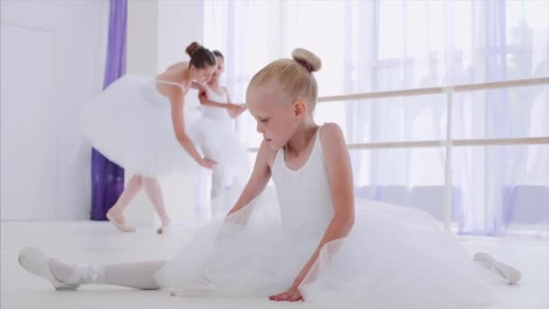 Criança menina bailarina em tutu branco está fazendo exercícios de alongamento na lição de balé . — Vídeo de Stock