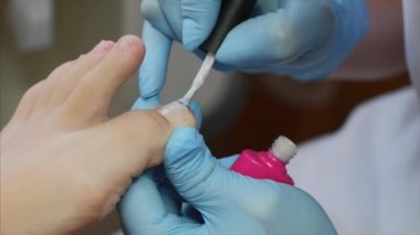 Pedikür ustası güzellik salonunda pembe ten rengi shellac kullanarak ayak tırnakları boyar.