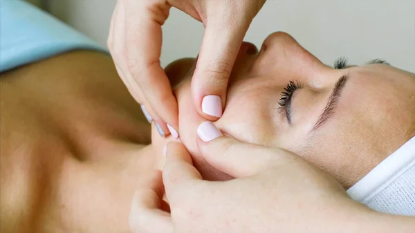 Masaj terapisti kozmetolojist güzellik kliniğinde kadın için yüz masajı yapar.