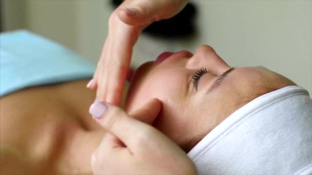 Massage therapist cosmetologist makes cheeks massage for woman in beauty salon. — Stock Video