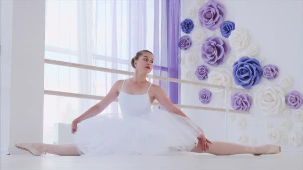 Bailarina en tutú blanco y pointes se estira sentada sobre cordel en clase de ballet . — Vídeos de Stock