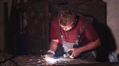 Kaynakçı yavaş çekimde koruyucu maske olmadan atölyede metal çit kaynak.