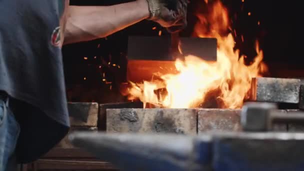 Працівник кидає вугілля в вогонь з молотком на ковадлі на передньому плані . — стокове відео