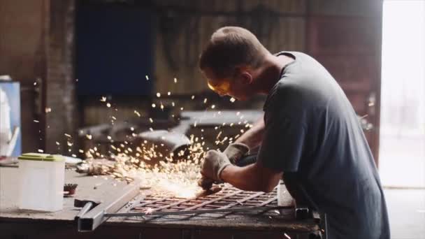 Locksmith grinds metal product after welding using angle grinder in forge shop. — Stock Video