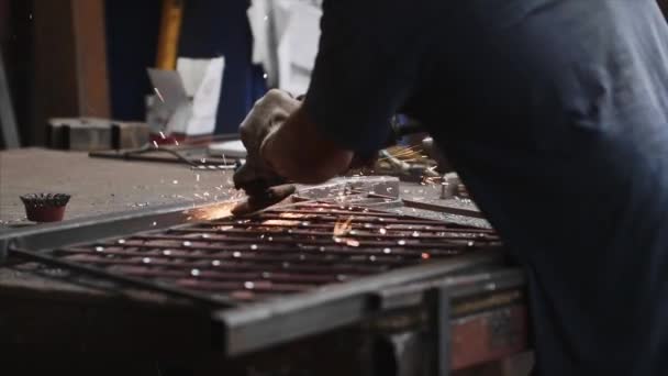 Serrurier broie le produit métallique après soudage à l'aide d'une meuleuse d'angle dans un atelier de forge . — Video