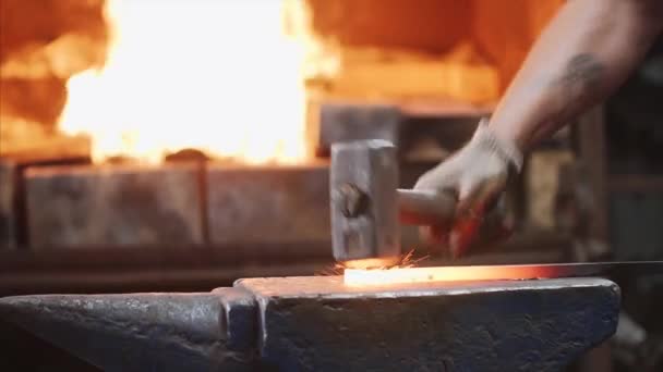 Blacksmith hitting hot metal bar with massive hammer on anvil.