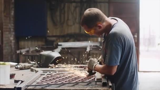 Serrurier broie le produit métallique après soudage à l'aide d'une meuleuse d'angle dans un atelier de forge . — Video