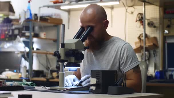 Técnico está soldando microchip mirando a través del microscopio en el centro de servicio . — Vídeos de Stock