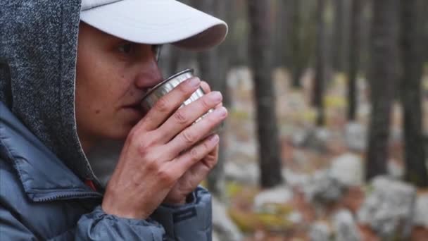 Retrato de primer plano de una joven excursionista bebiendo té de una taza de metal en el bosque . — Vídeo de stock