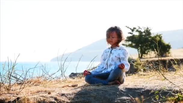 Linda criança gurl meditando sozinho em pose de lótus na margem do lago — Vídeo de Stock