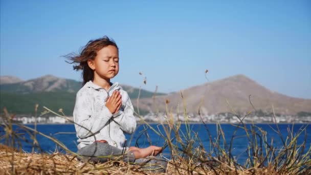 Carino piccolo bambino gurl meditando da solo in posa loto sulla riva del lago — Video Stock