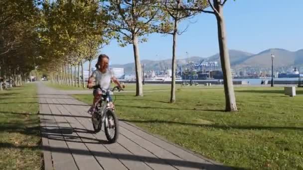 O fetiță se plimbă cu bicicleta de-a lungul aleii mării, împușcat de echilibru . — Videoclip de stoc