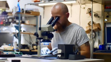 Teknisyen servis merkezinde mikroskoptan bakan mikroçip lehimiyor.