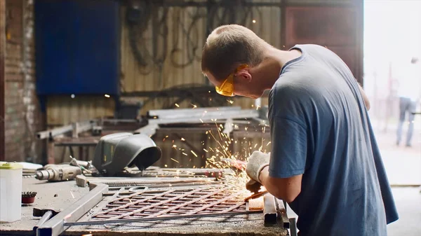 Locksmith grinds metal product after welding using angle grinder in forge shop.