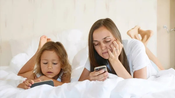 Ung mamma med liten Söt dotter använder prylar som ligger på en vit säng. — Stockfoto