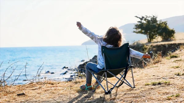 Маленькая девочка, сидящая на стуле на берегу моря и растягивающаяся рано утром — стоковое фото