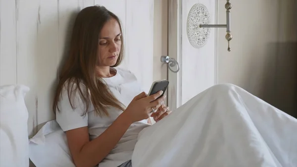Молодая женщина с помощью смартфона в спальне по утрам — стоковое фото