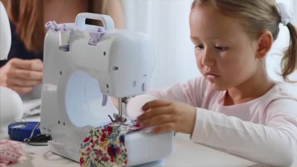 Malá holčička šití tkaninu a mluvení. Máma je na pozadí. Close-up. — Stock video