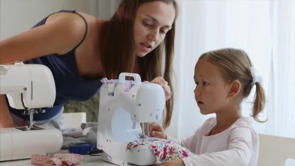 Uma rapariga está a costurar numa máquina. A mãe mostra como trabalhar com equipamentos. Close-up . — Vídeo de Stock