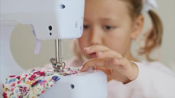 Malá holka šije tkaniny. Ruce a šicí stroj v ohnisku. Detailní záběr. — Stock video