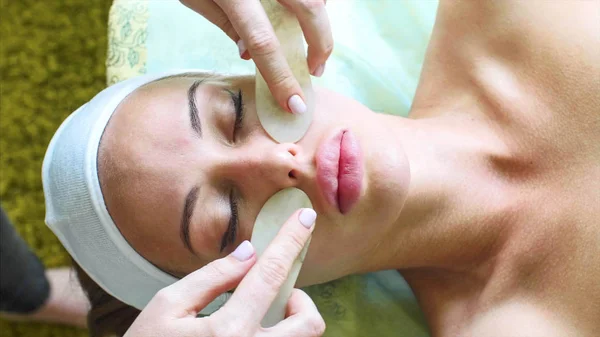 Woman receives facial massage with special stones in cosmetology spa center. — Stock Photo, Image