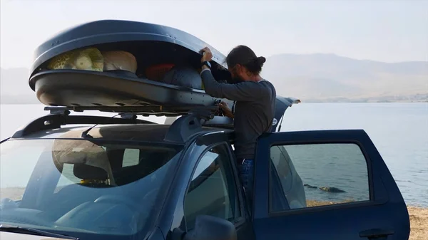Genç sakallı adam araba çatı kutusundan bir kamp ekipmanları dışarı alıyor — Stok fotoğraf
